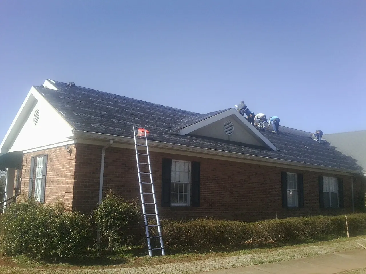 Crew tearing shingles off a brick ranch roof with a ladder set — Emergency Roof Repair work by our crew in Barton