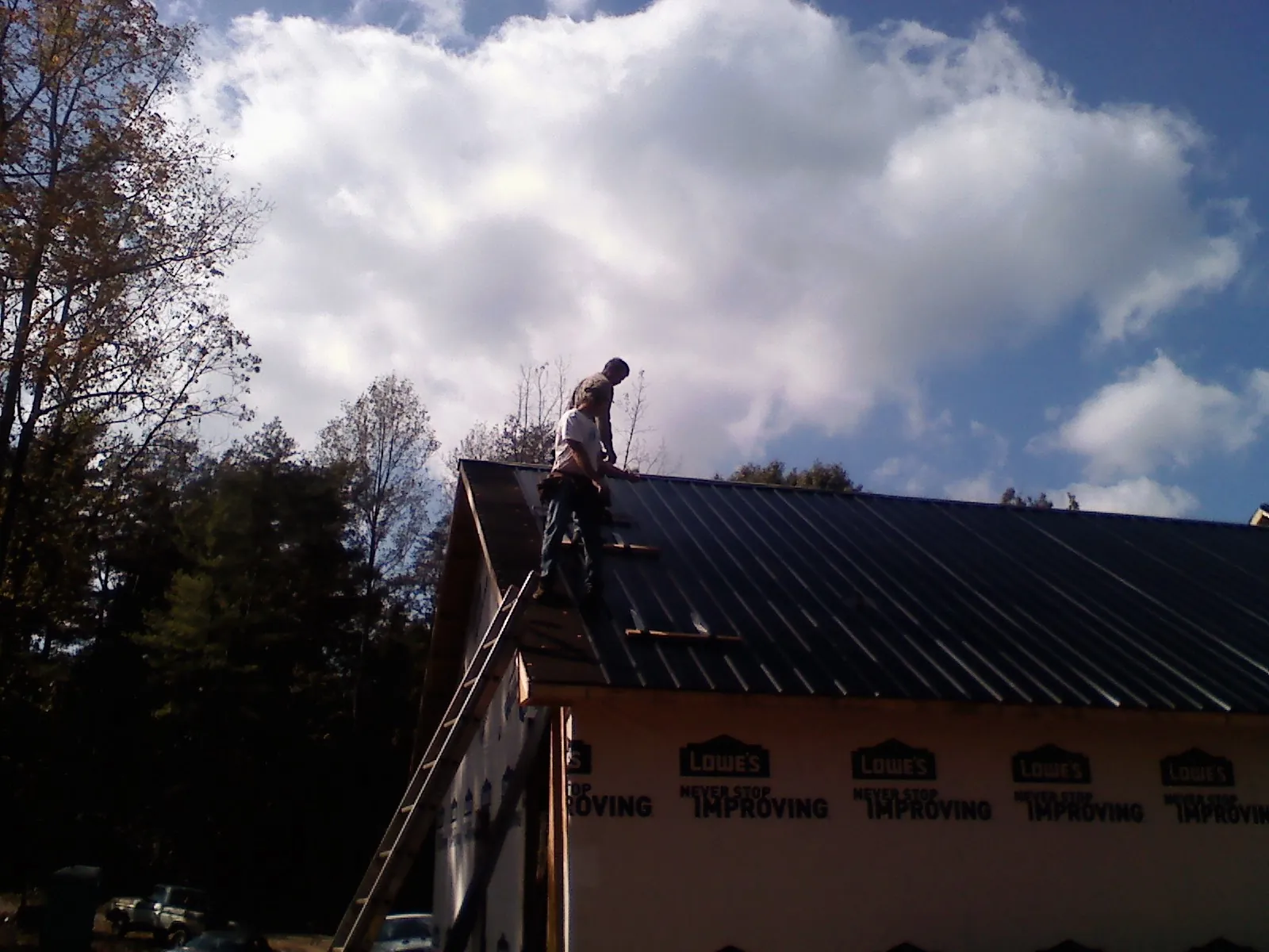 Roofer fastening dark metal panels high against a cloudy sky, from a Roof Inspection job in Barton