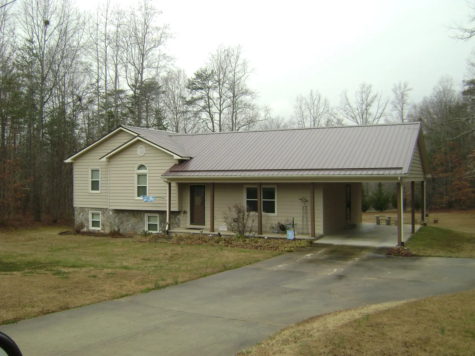 Brown metal roof on a tan split level home with an attached carport in Barton
